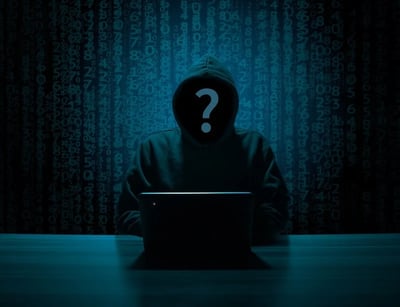 Man in black hoodie with question mark instead of face using computer in dark room