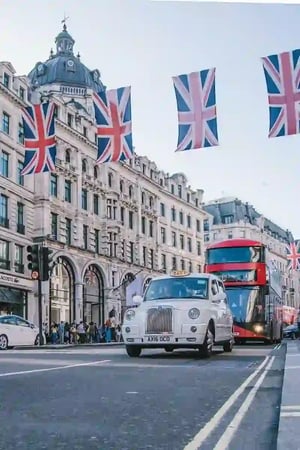 Old car and two level bus on street near to the old building with British flags