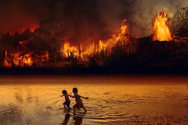 Two girls running in the water, with the forest burning in the background
