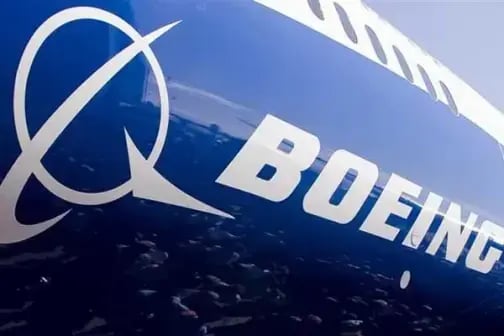 Primer plano de un logotipo de Boeing en el fuselaje de un avión con una vista aérea borrosa del océano al fondo.